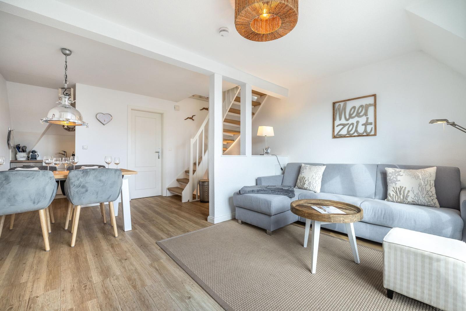 Living and dining area with sofa, table and chairs. Staircase and wall decoration visible.
