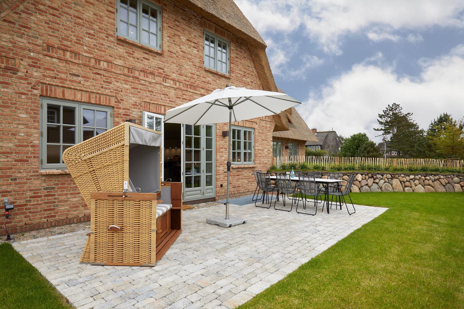 Terrasse mit Loungemöbeln, Sonnenschirm und Gartenhaus an einem traditionellen Haus.