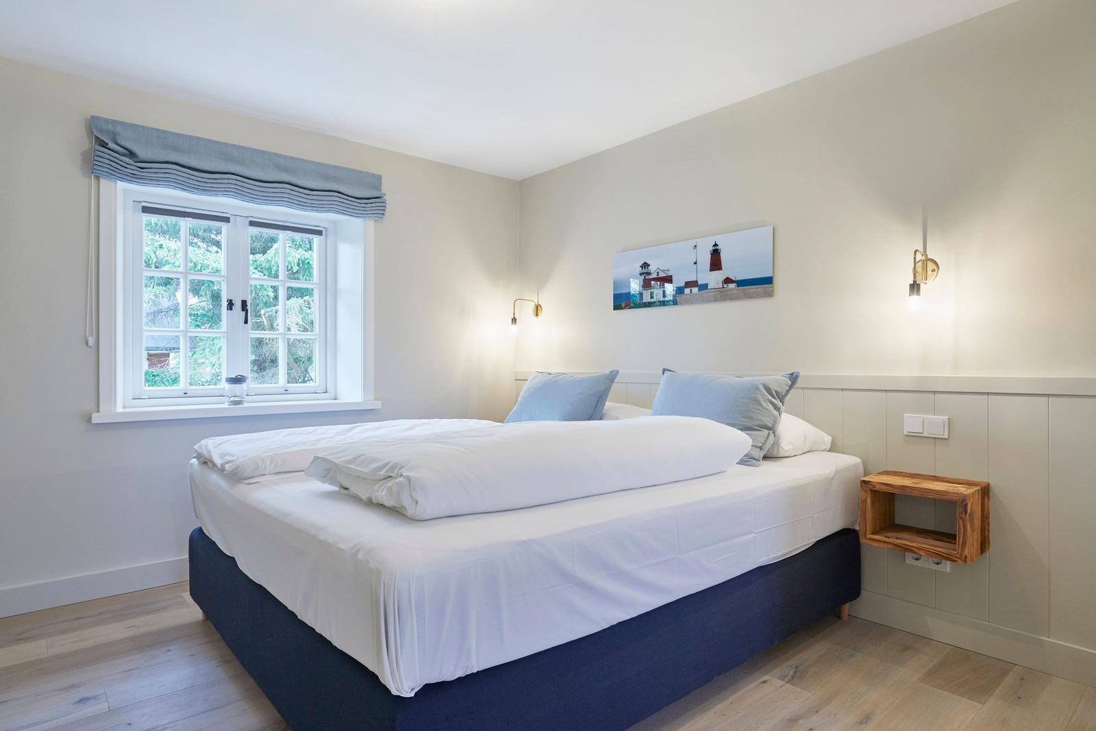 Schlafzimmer mit Bett, Fenster und Wandbild.