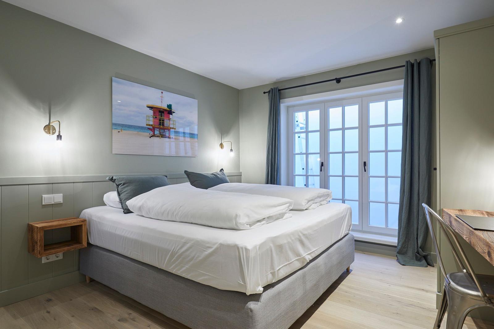 Schlafzimmer mit Doppelbett, Fenster und Wandbild.