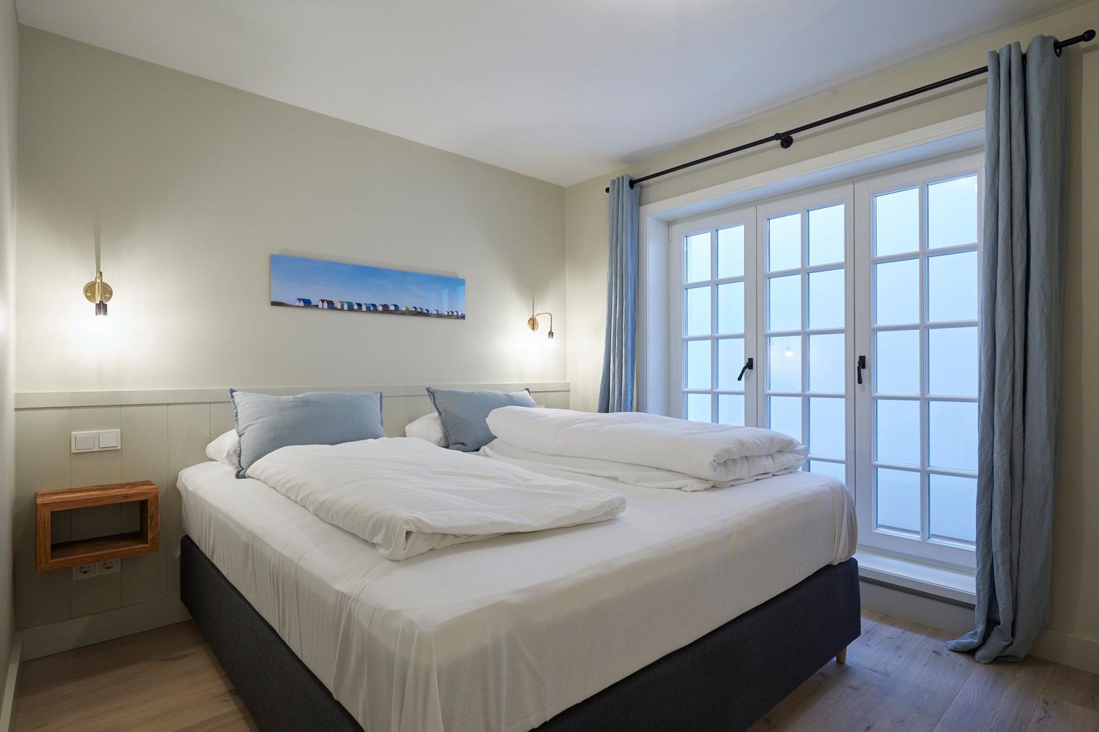 Schlafzimmer mit Doppelbett, Fenster und Wandbild.