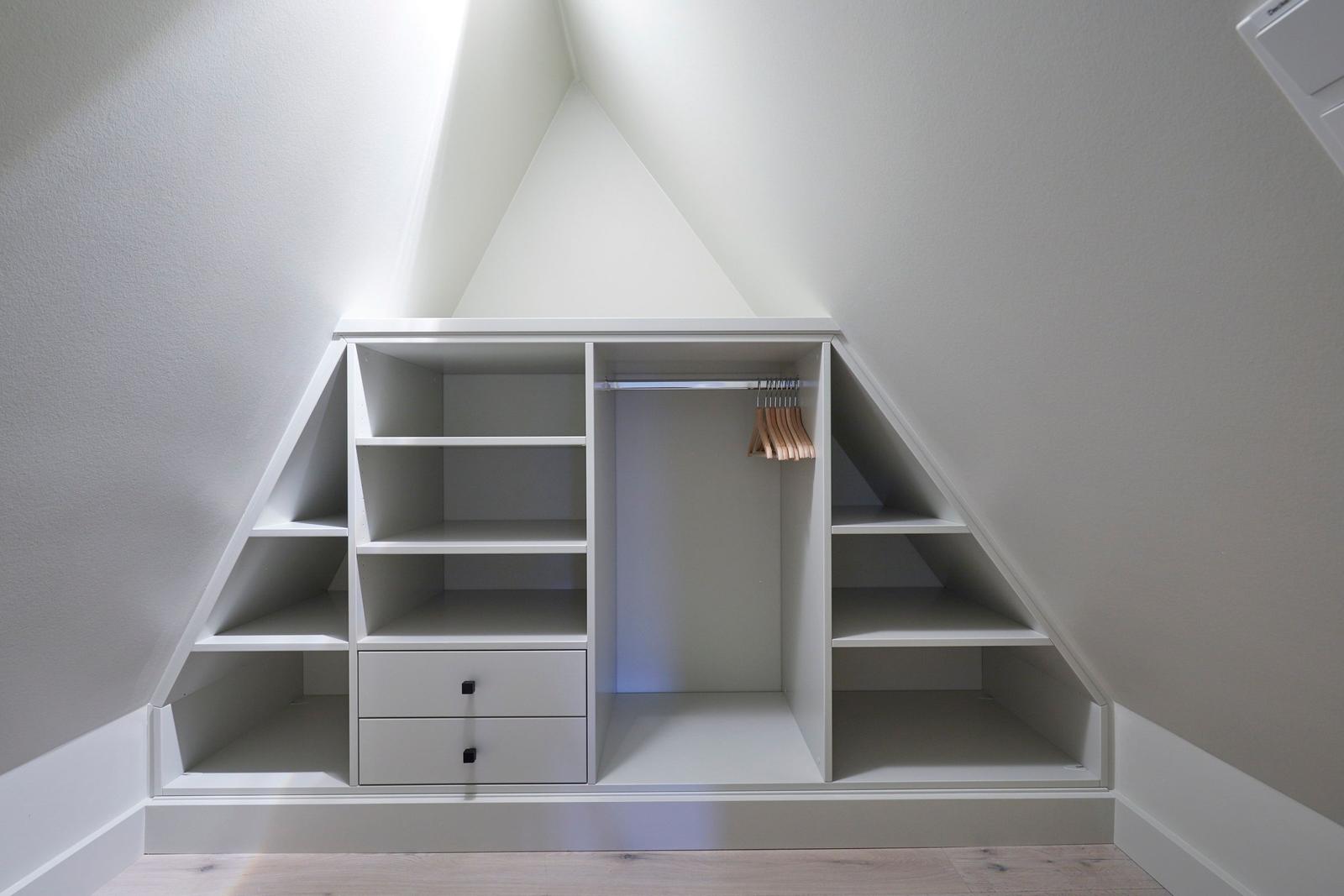 Ein weißer Schrank mit Regalen und Kleiderstange unter einem Dach