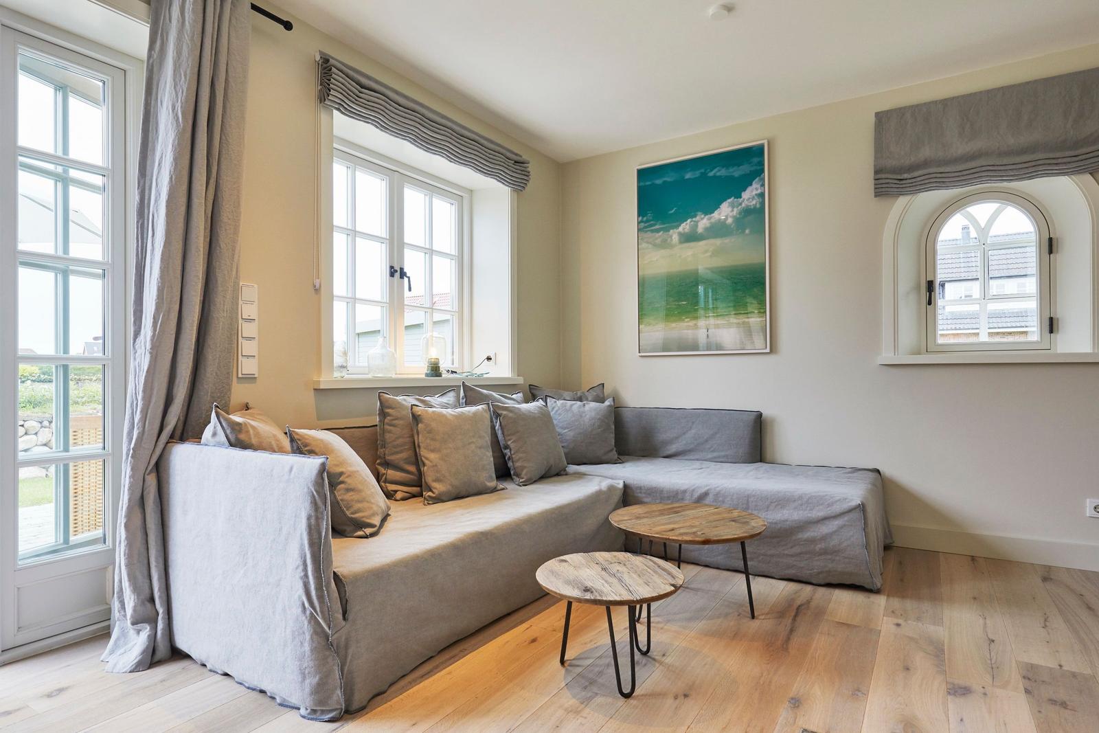 Wohnzimmer mit grauem Sofa, Holzboden und Fenstern.