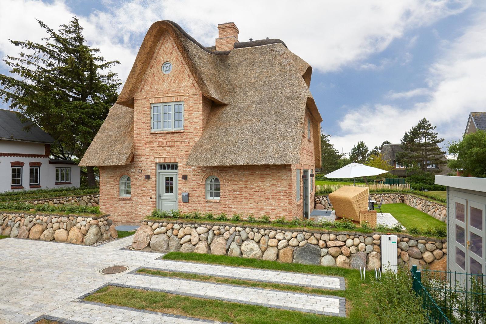 Haus mit Strohdach, Steinmauer und Gartenbereich mit Liege.