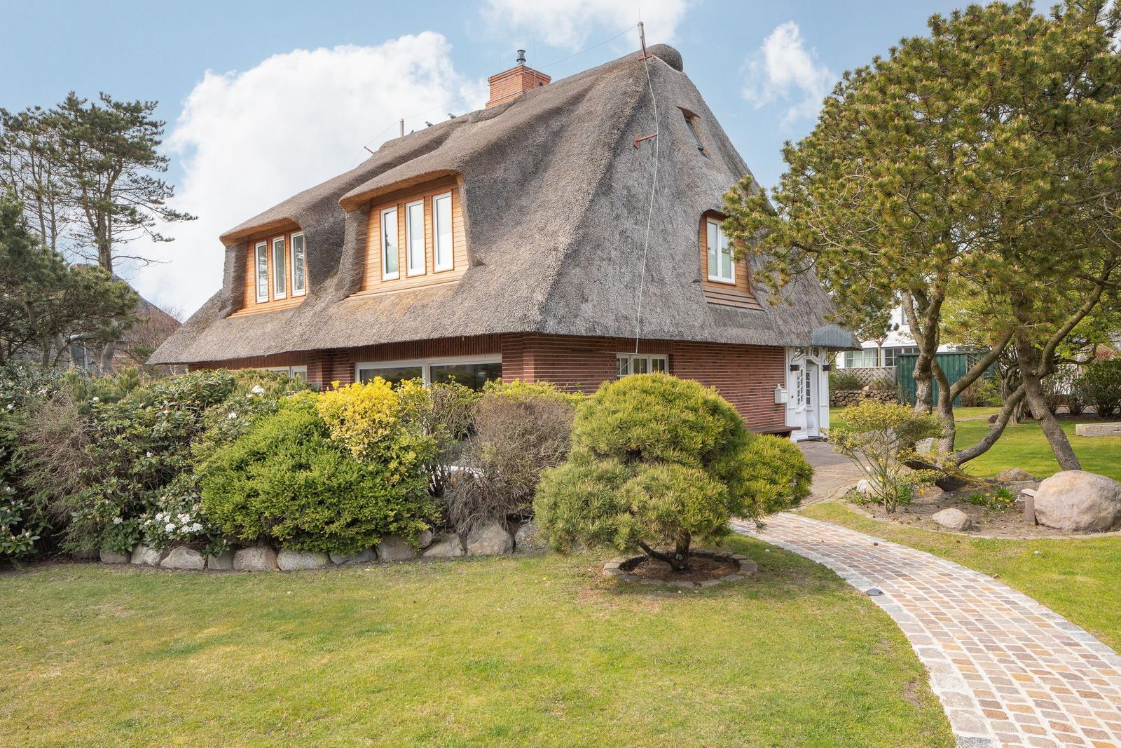 Haus mit Strohdach, gepflegter Garten und Steinweg.