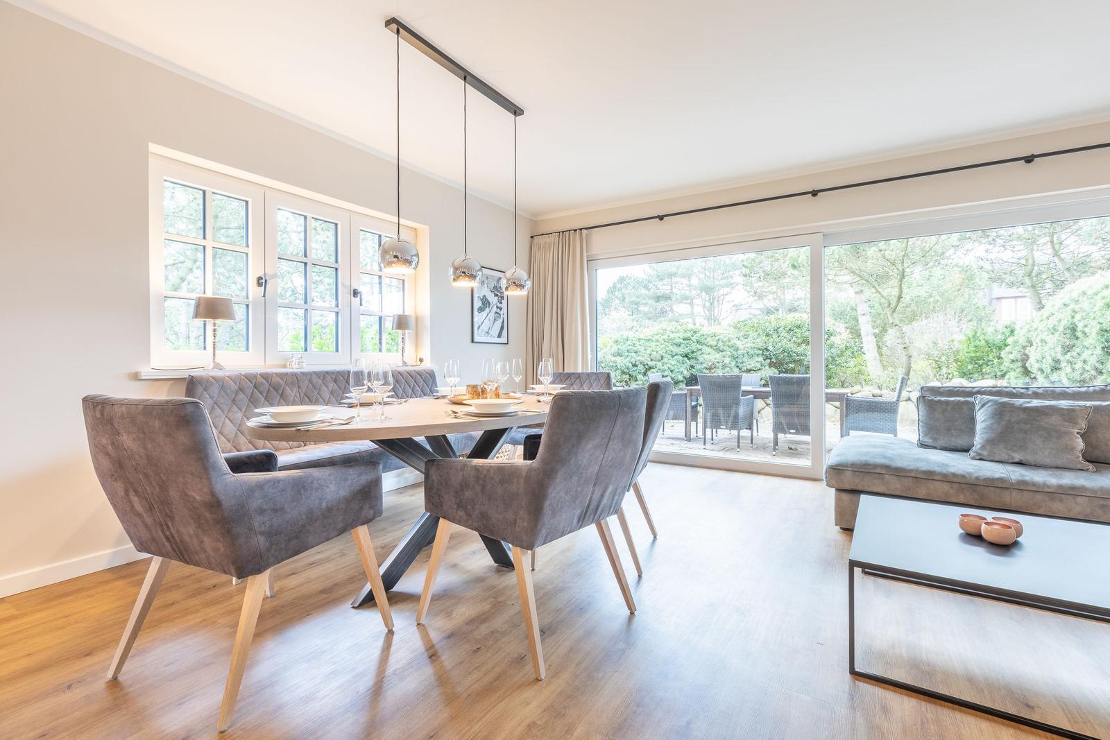 Essbereich mit Tisch und Stühlen. Wohnbereich mit Sofa und Couchtisch. Glasfront zum Garten.