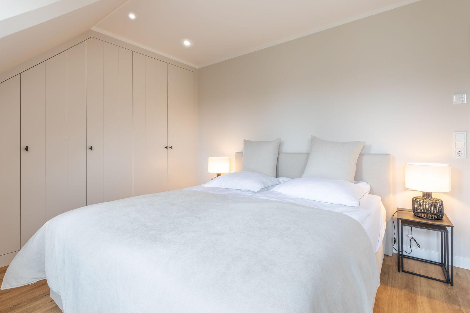 Schlafzimmer mit Doppelbett, Nachttischen und Kleiderschrank unter Dachschrägen.