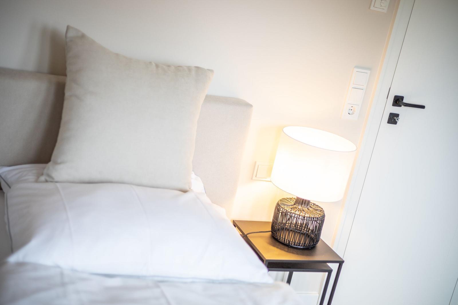 Bettkopfteil mit Kissen, Nachttisch und Lampe neben Tür