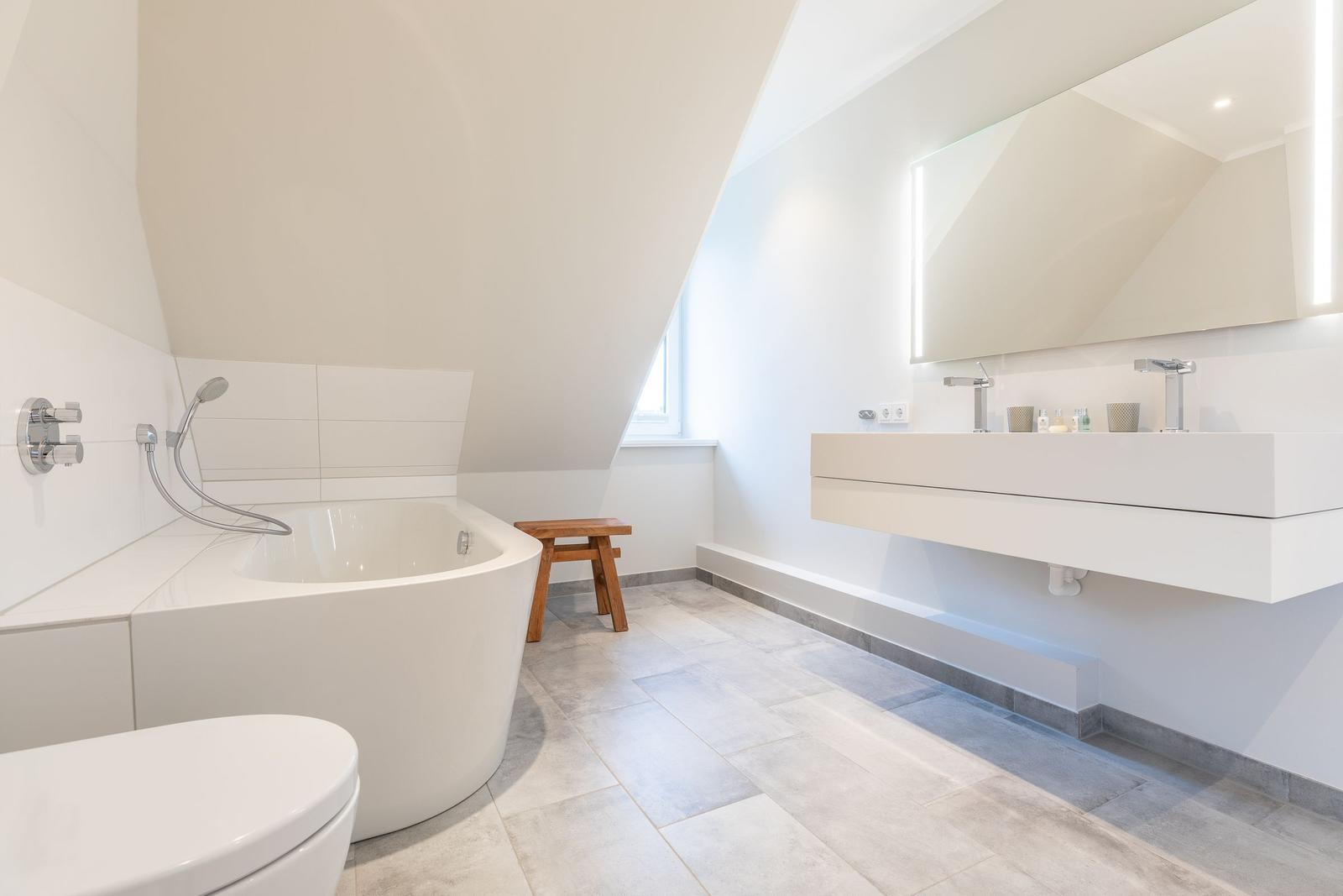 Badezimmer mit freistehender Badewanne, Waschbecken und Toilette unter schräger Decke.