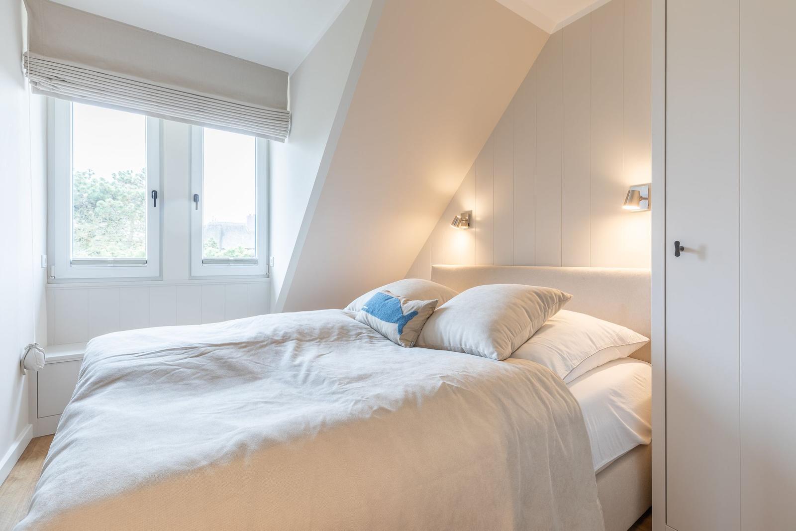 Schlafzimmer mit Dachschrägen, Fenster und Bett.