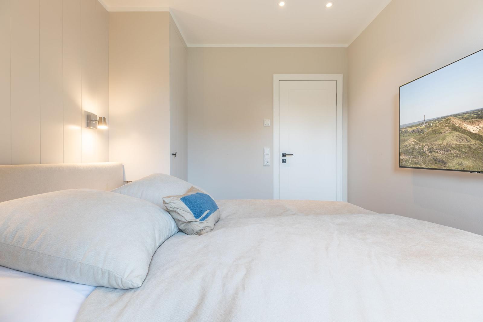 Schlafzimmer mit Bett, Wandlampe und Fernseher an der Wand.