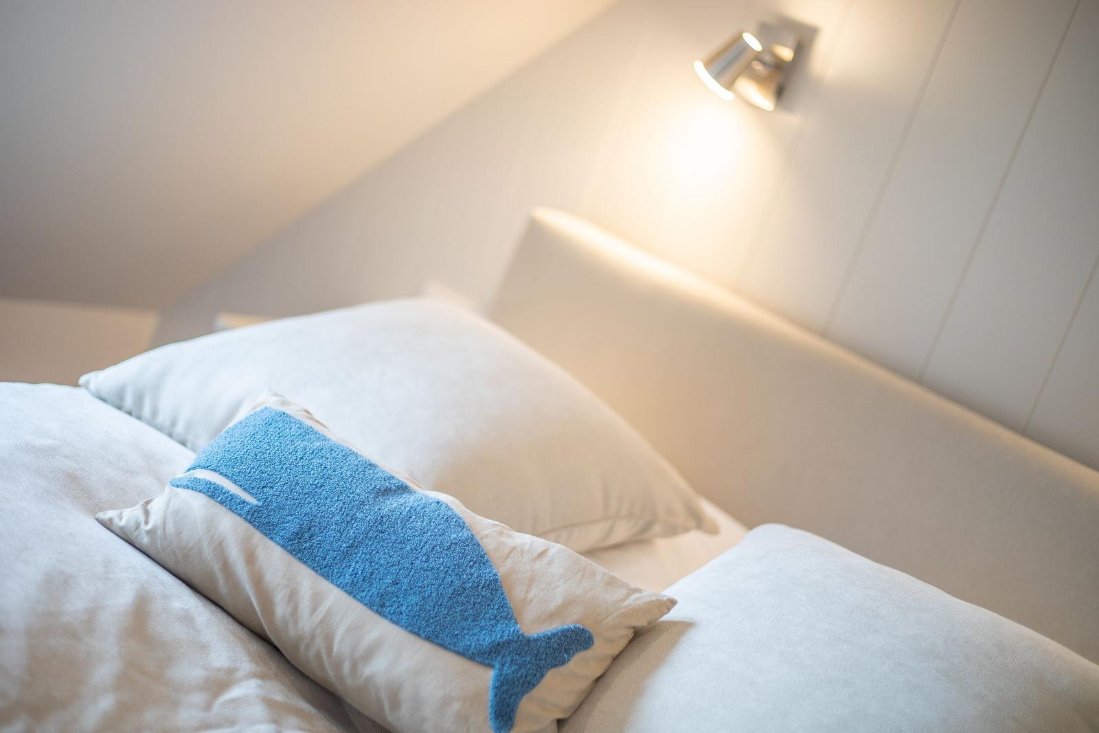 Schlafzimmer mit Bett, Kissen und Wandlampe.