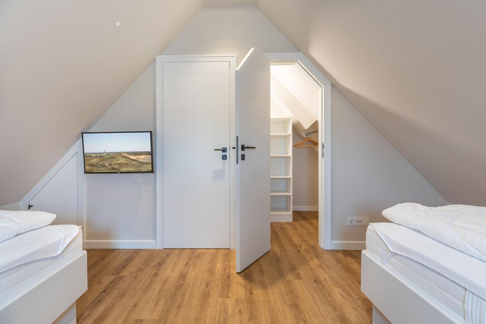 Zimmer mit zwei Betten, TV und Kleiderschrank. Holzboden und schräge Decke.