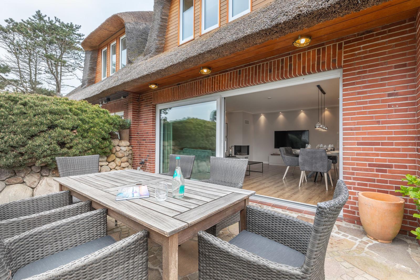 Terrasse mit Tisch und Stühlen, Blick ins Haus mit Essbereich.