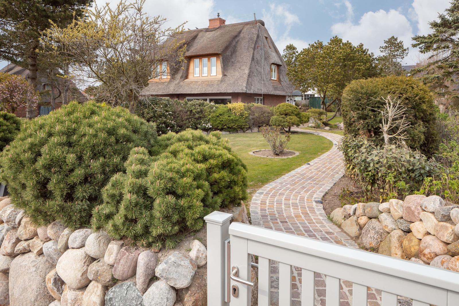 Haus mit Strohdach, gepflasterter Weg und Garten mit Steingarten.