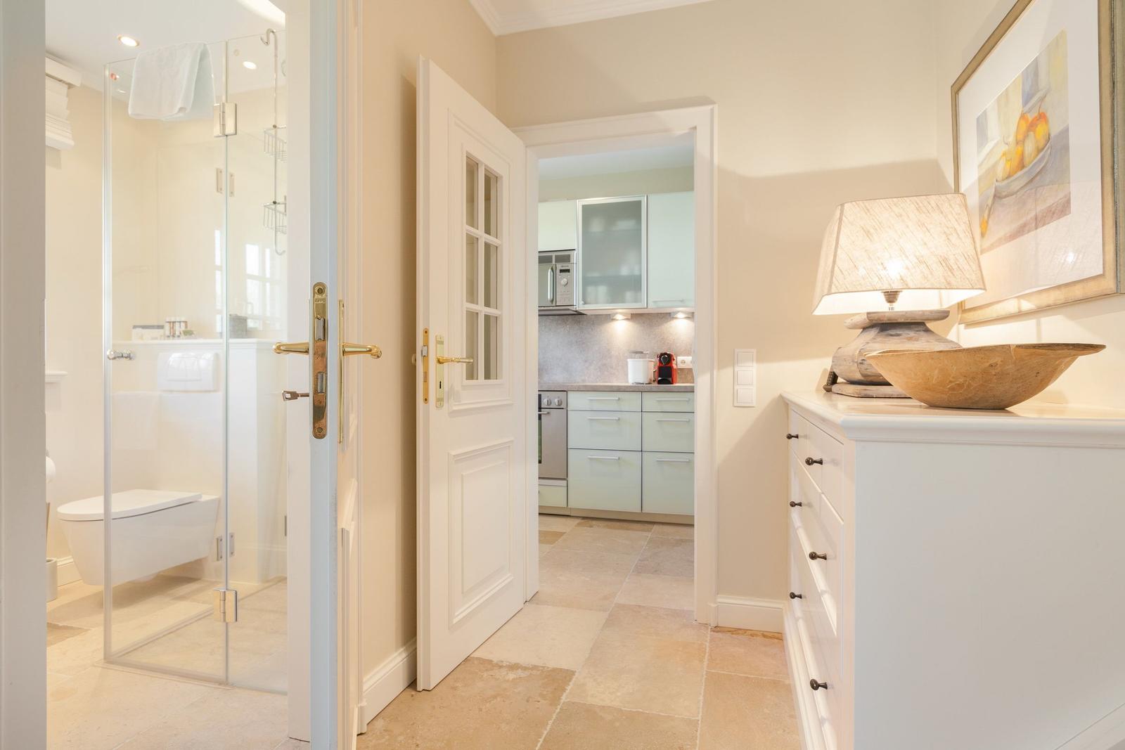 Hallway with bedroom, kitchen, and bathroom. White furniture and stone tiles.
