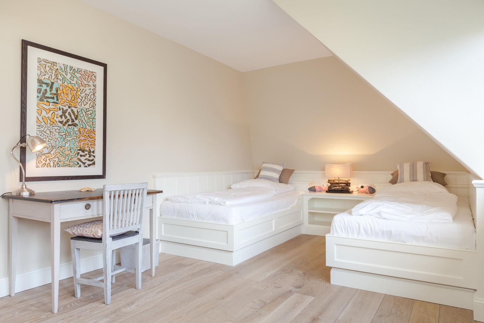 Two beds, desk, and wall art in an attic room.