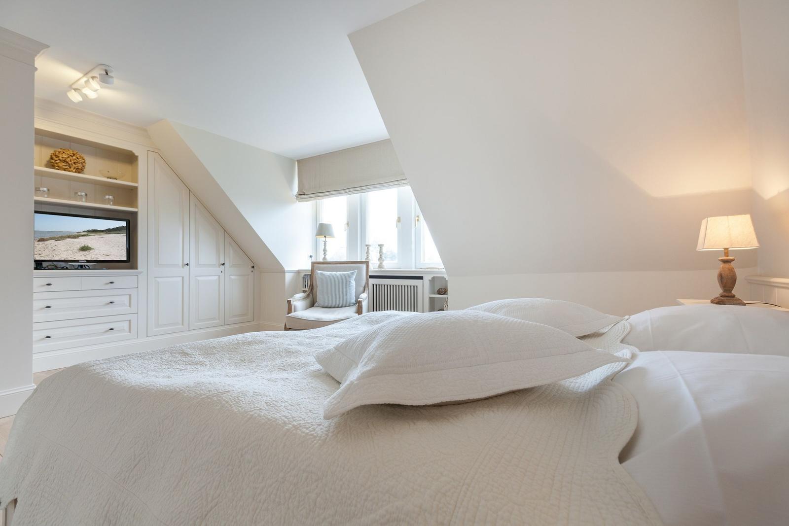 Bedroom with sloped ceiling, bed, TV, and armchair.