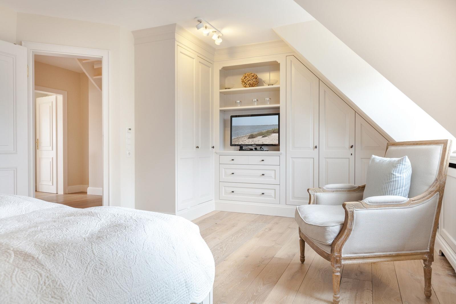 Bedroom with sloped ceiling, white closet, and armchair.