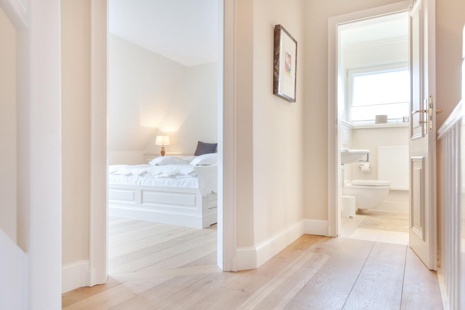 Bedroom and bathroom accessible via hallway. Wooden floor and white walls.