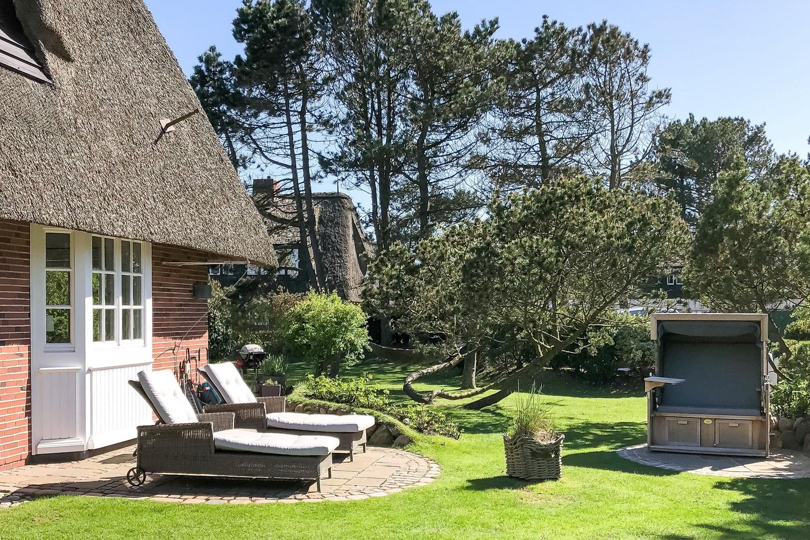 House with thatched roof, garden with loungers and pavilion.
