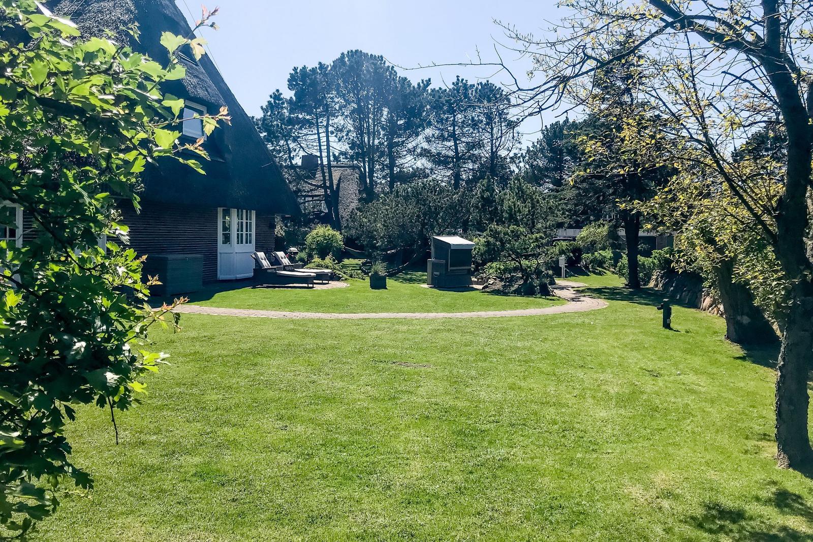 Green lawn with sun loungers in front of a house with thatched roof.