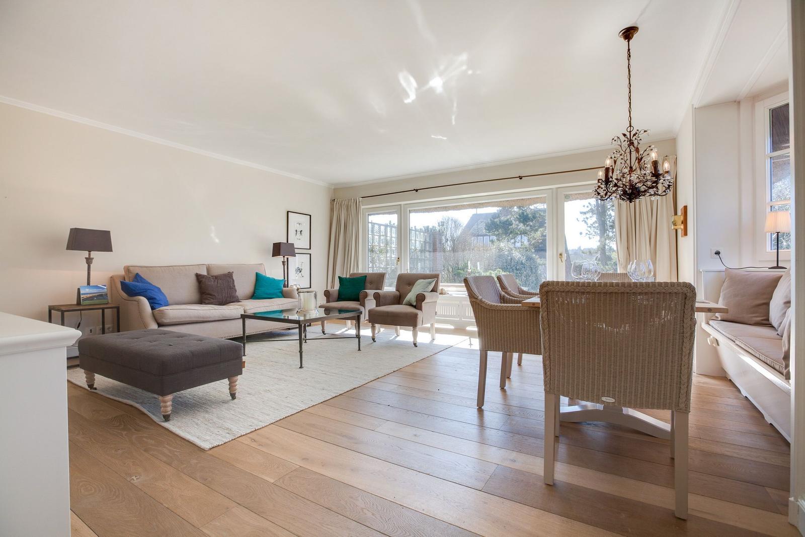 Living and dining area with wooden floor, sofa, chairs, and windows.