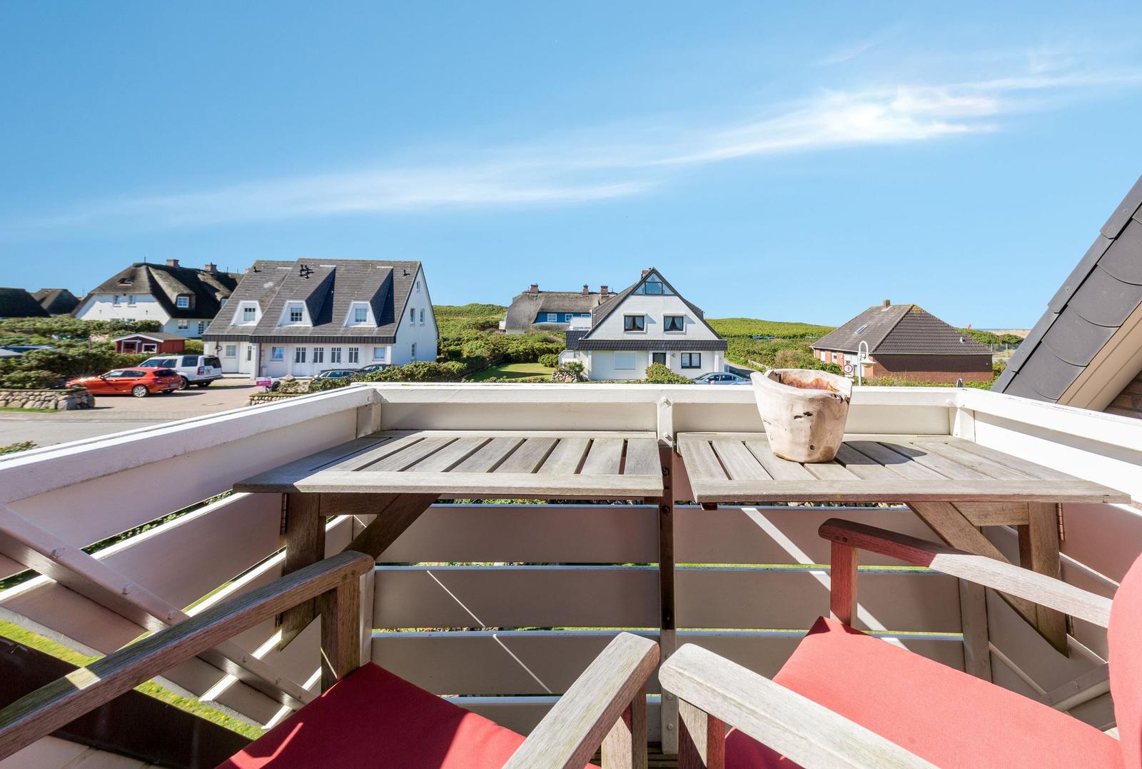 Terrasse mit Tisch und Stühlen, Blick auf Häuser und grüne Hügel.