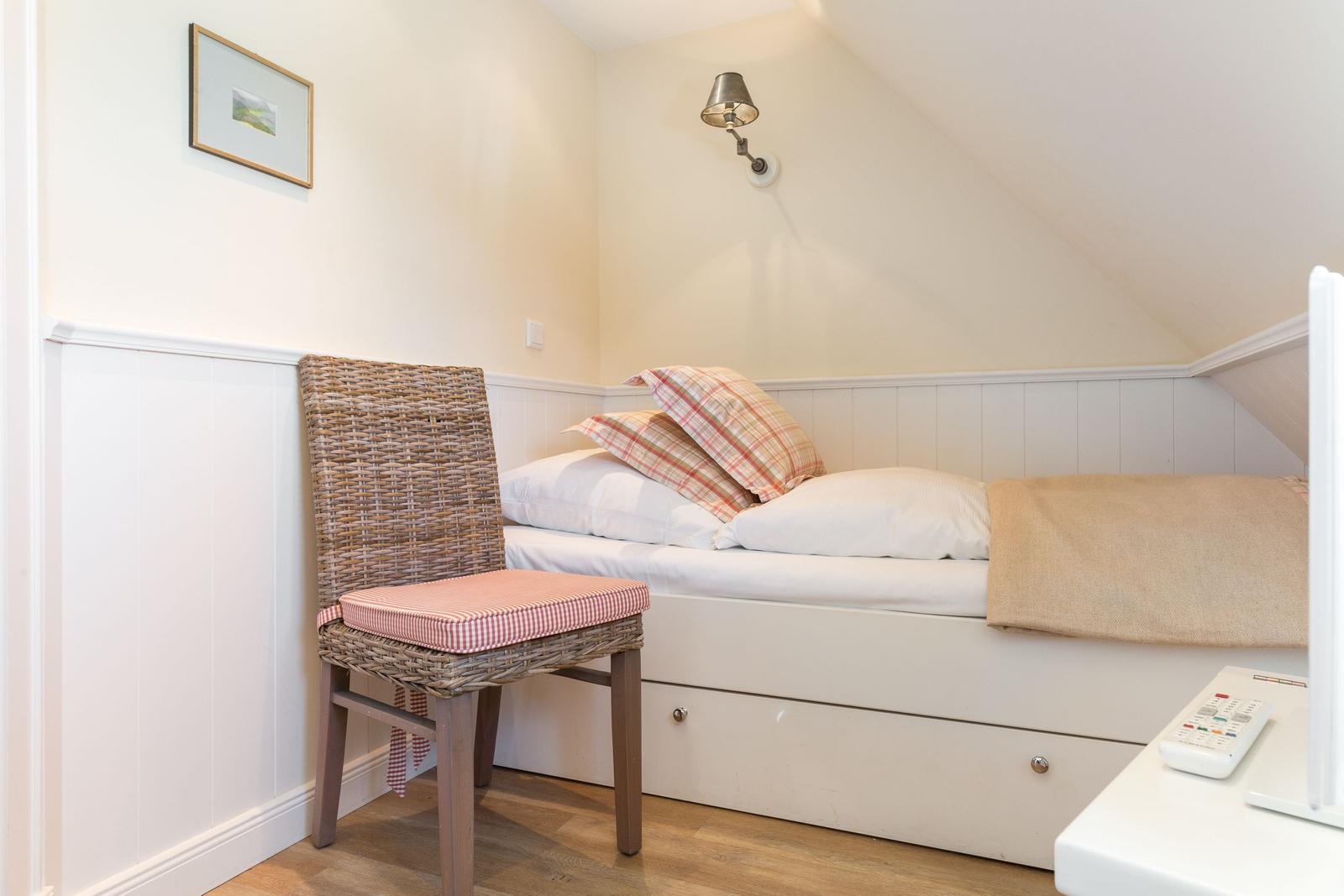 Schlafzimmer mit Bett, Stuhl und Wandlampe unter Dachschräge