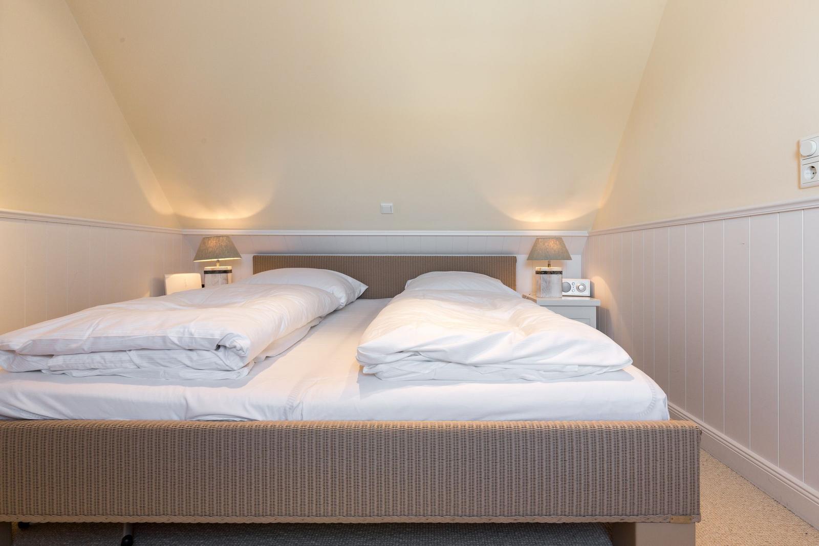 Zimmer mit Doppelbett, Nachttischen und Lampen unter schrägen Wänden.
