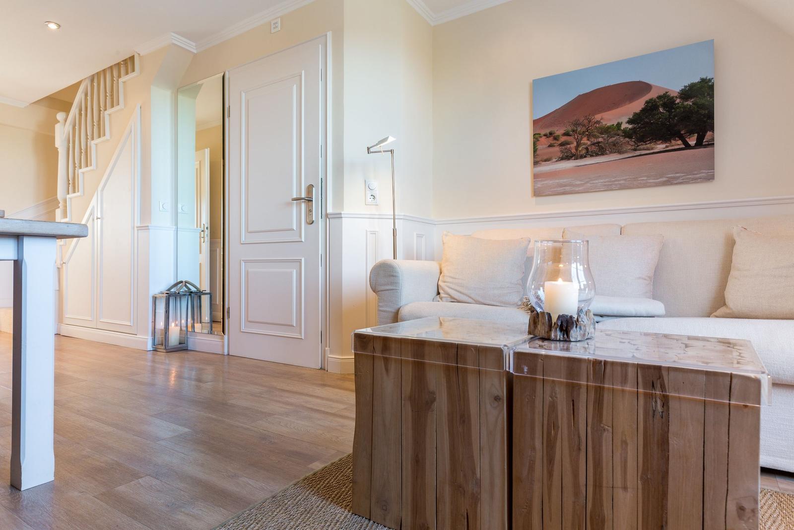 Wohnzimmer mit Sofa, Holztisch und Wandbild. Treppenhaus und Tür im Hintergrund.