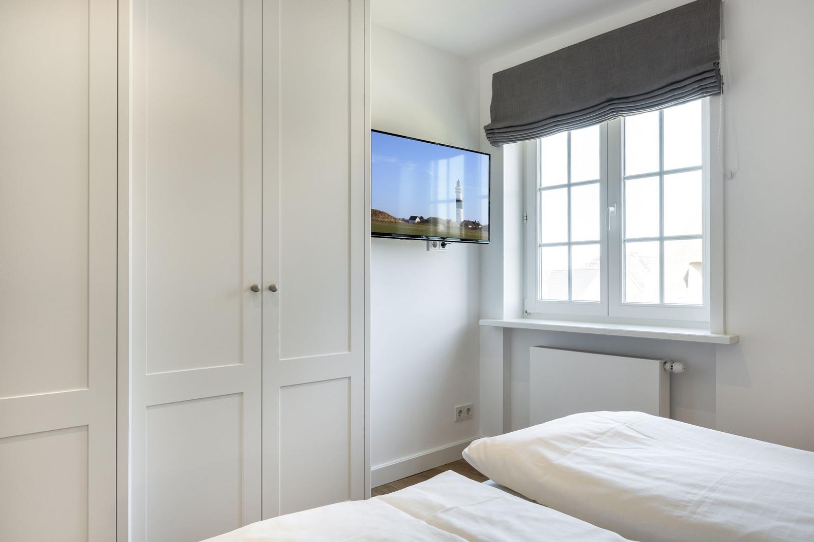 Bedroom with white bed, window, and wall-mounted TV.