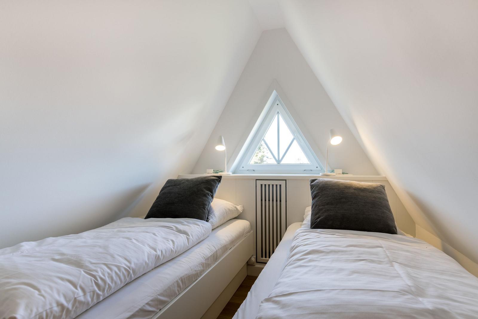 Two beds under a skylight with two nightstands and lamps.
