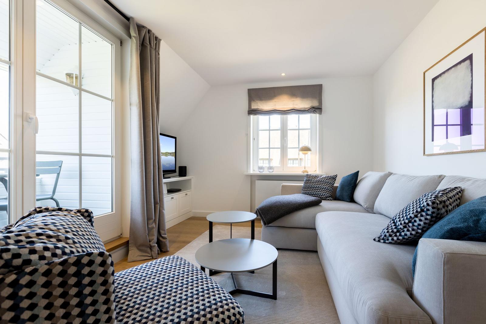 Living room with sofa, tables, and windows. Outdoor area visible.