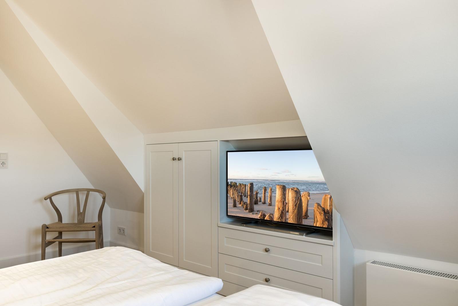 Bedroom with sloped ceiling, bed, chair, and TV showing beach.