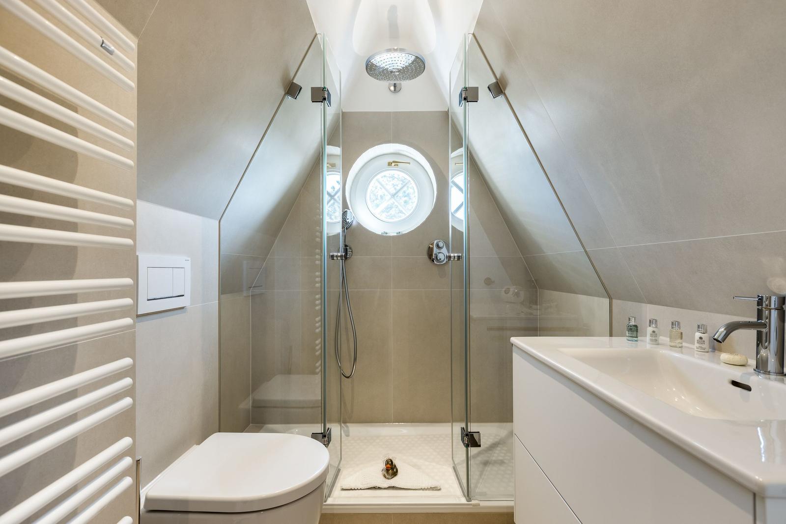 Shower with glass enclosure, round window, and sink with mirror.