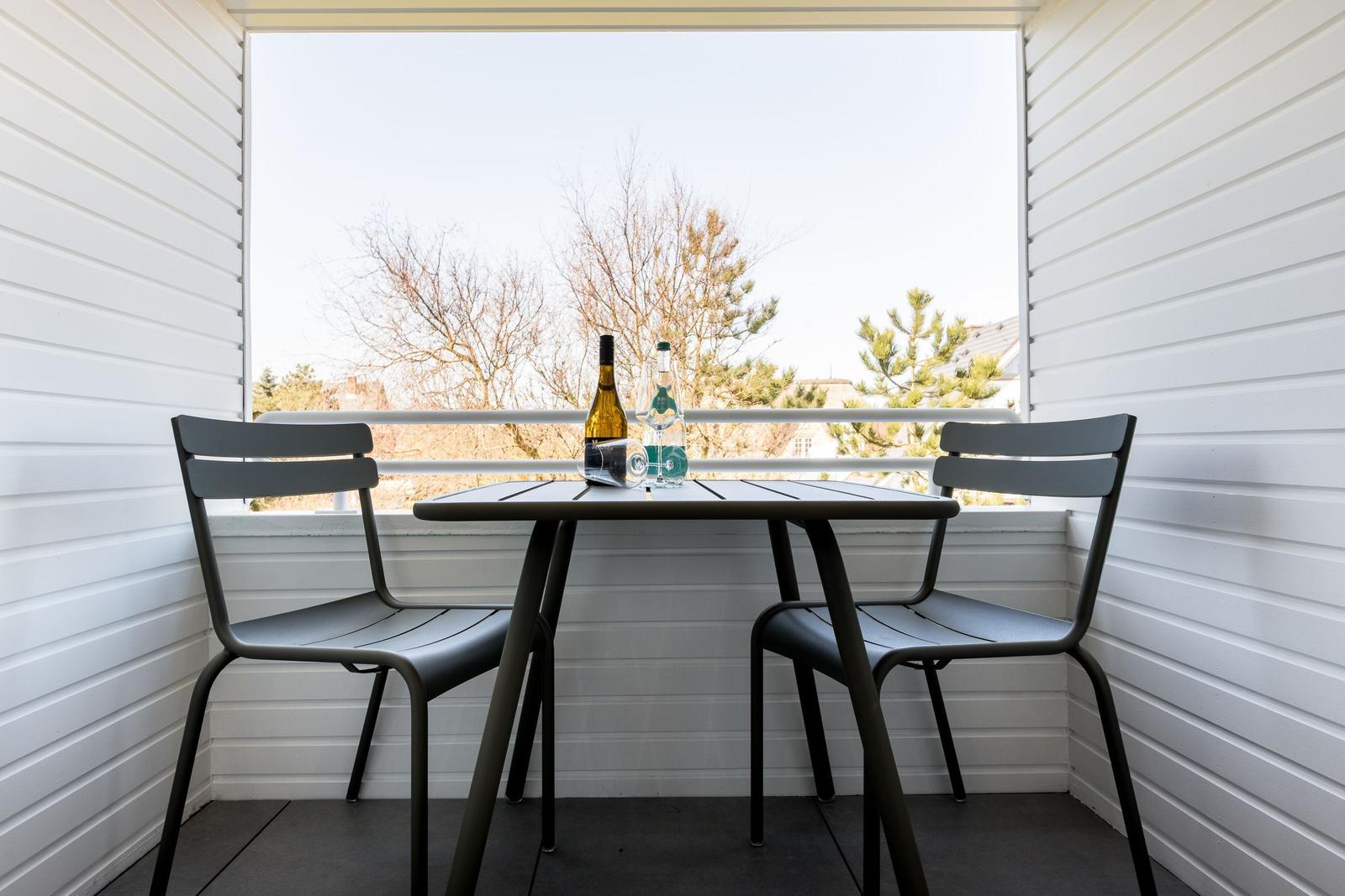 Balcony with table and two chairs, bottle and glass on table, view of trees.