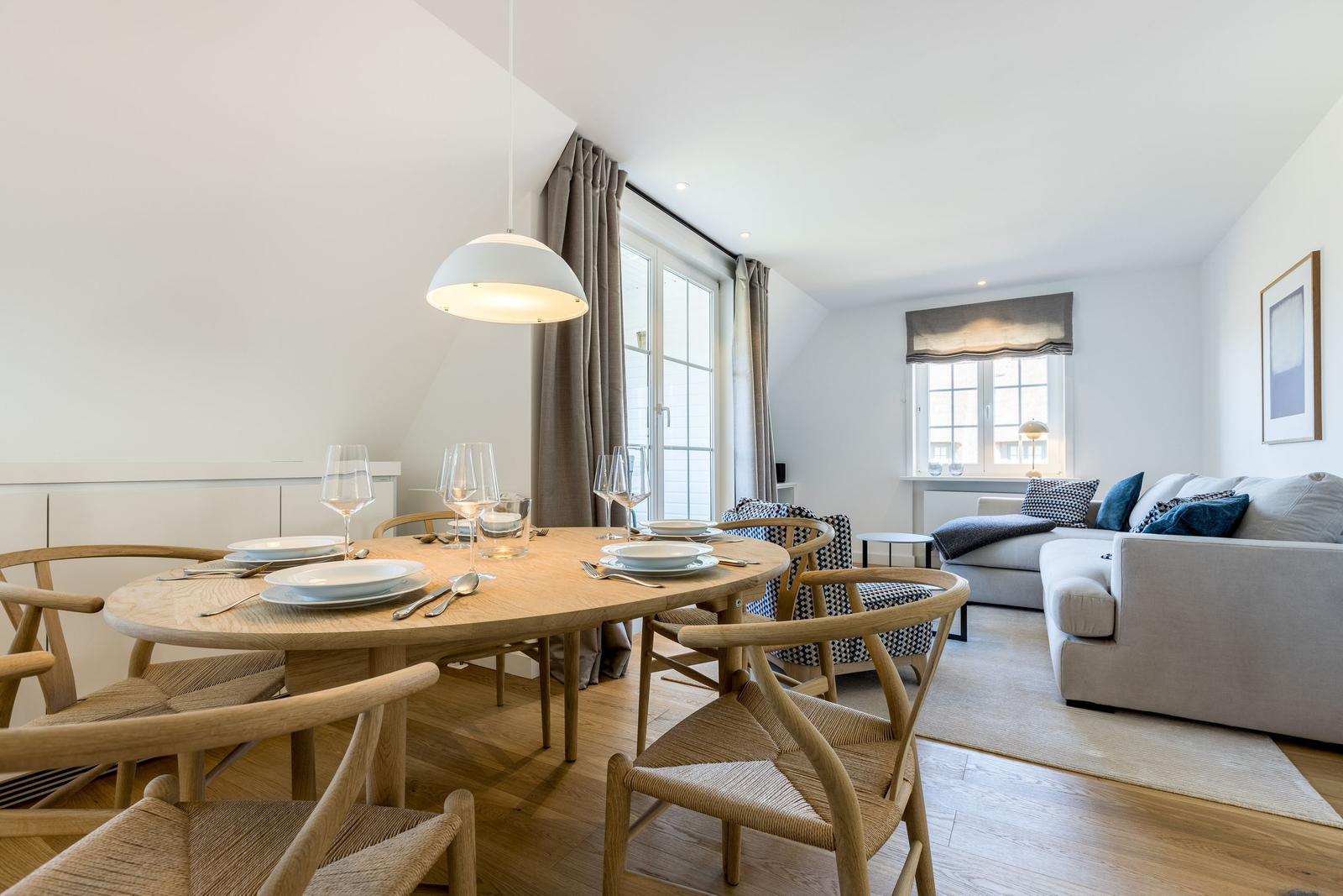 Dining area with round table and chairs. Living area with sofa and windows.