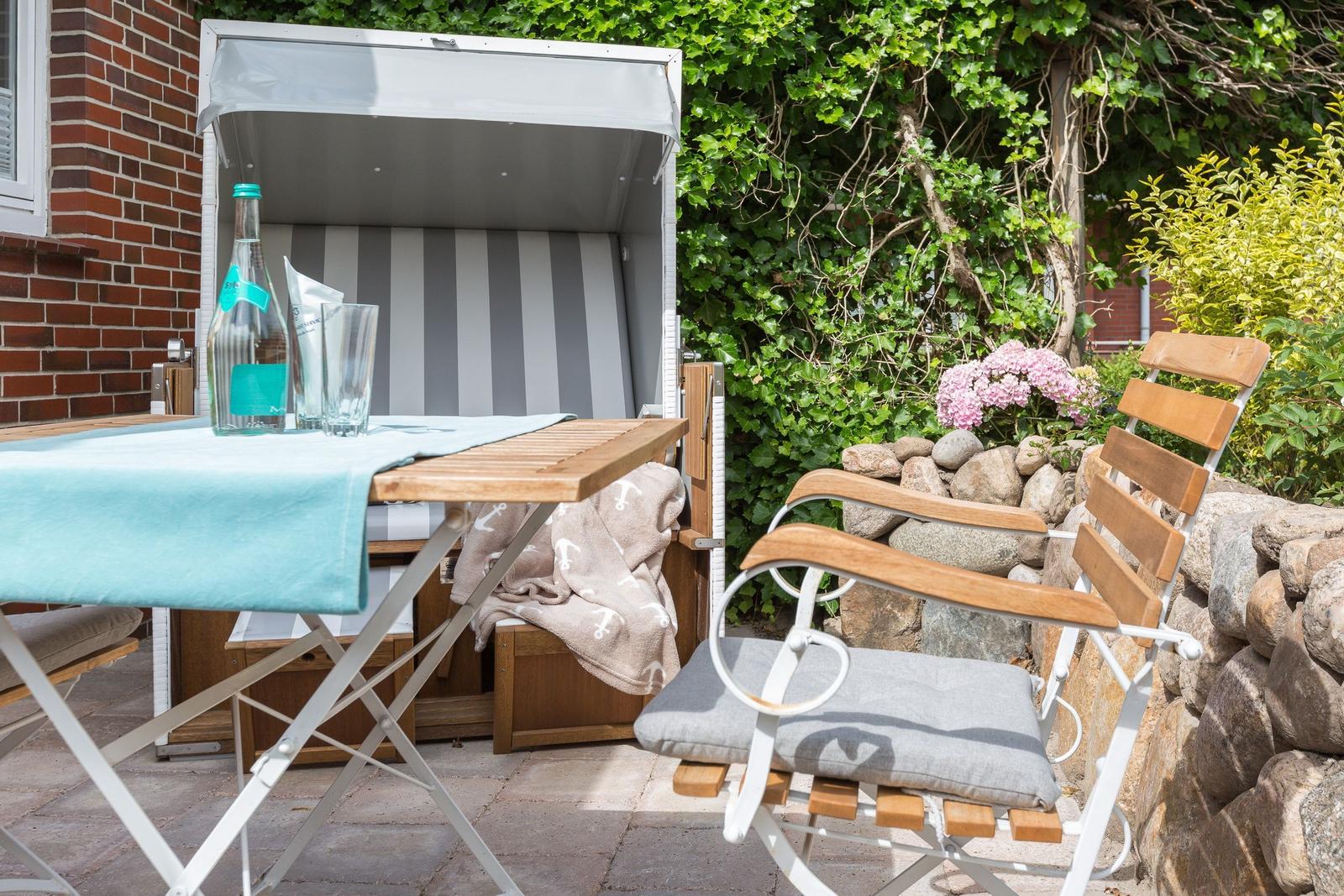 Outdoor area with beach chair, table, and chair. Background: green plants and stone wall.
