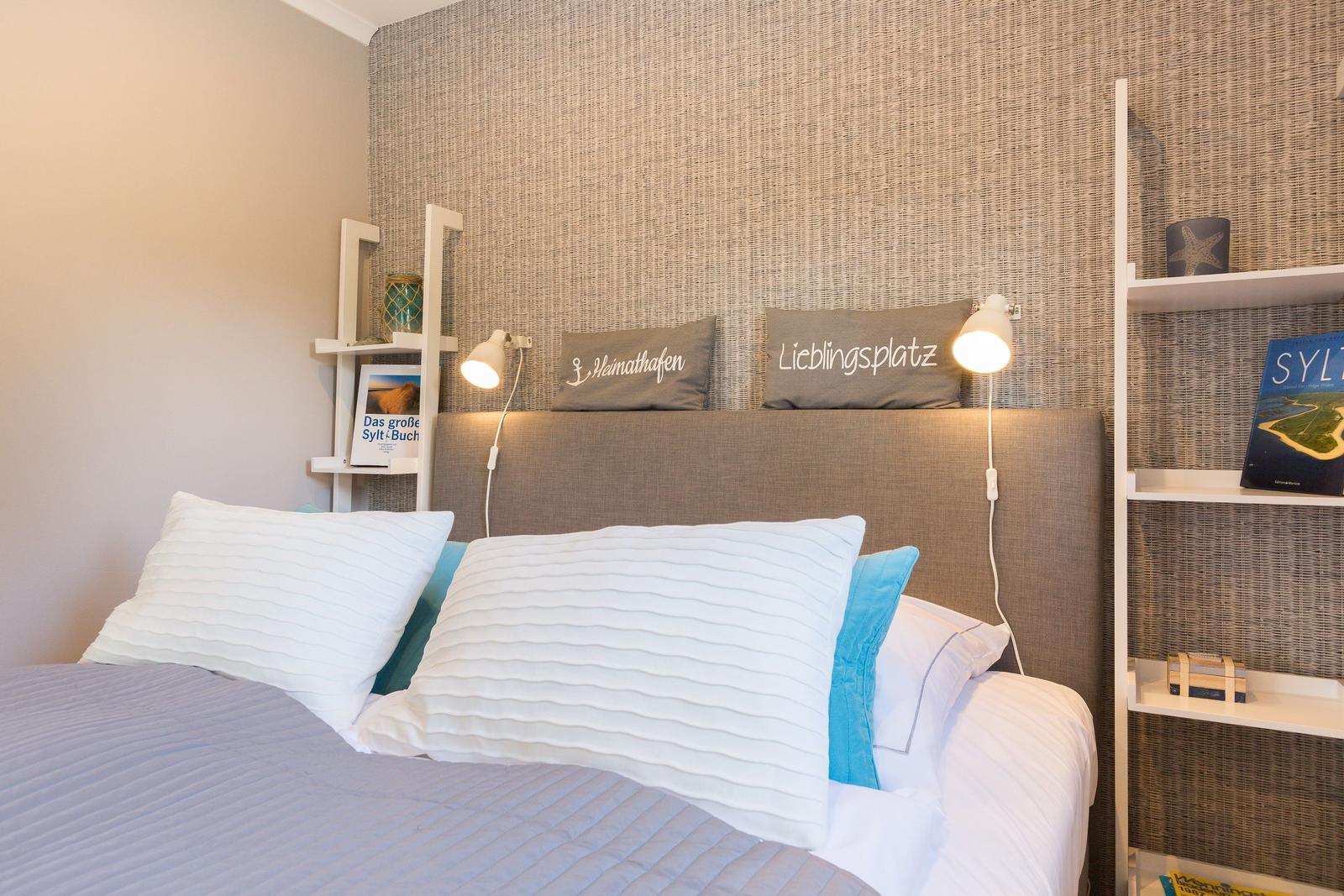 Bedroom with bed, pillows, and nightstands. Wall with textile covering and bookshelves.
