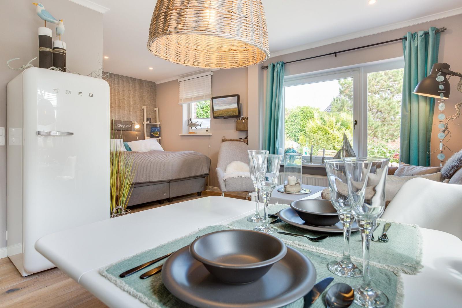 Dining room with table setting and garden view. Bedroom with bed in background.