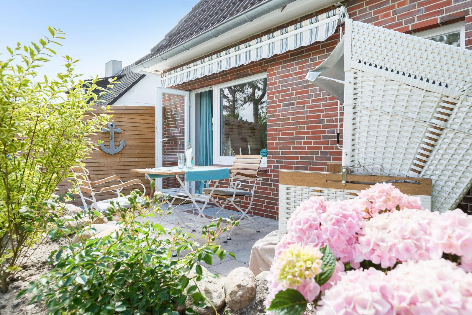 Terrace with table, chairs, and white awning in front of red brick house.