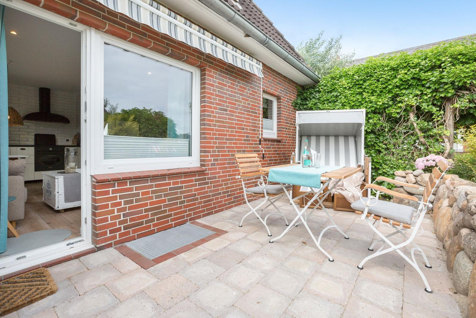 Terrace with table, chairs, and sunshade in front of red brick house.