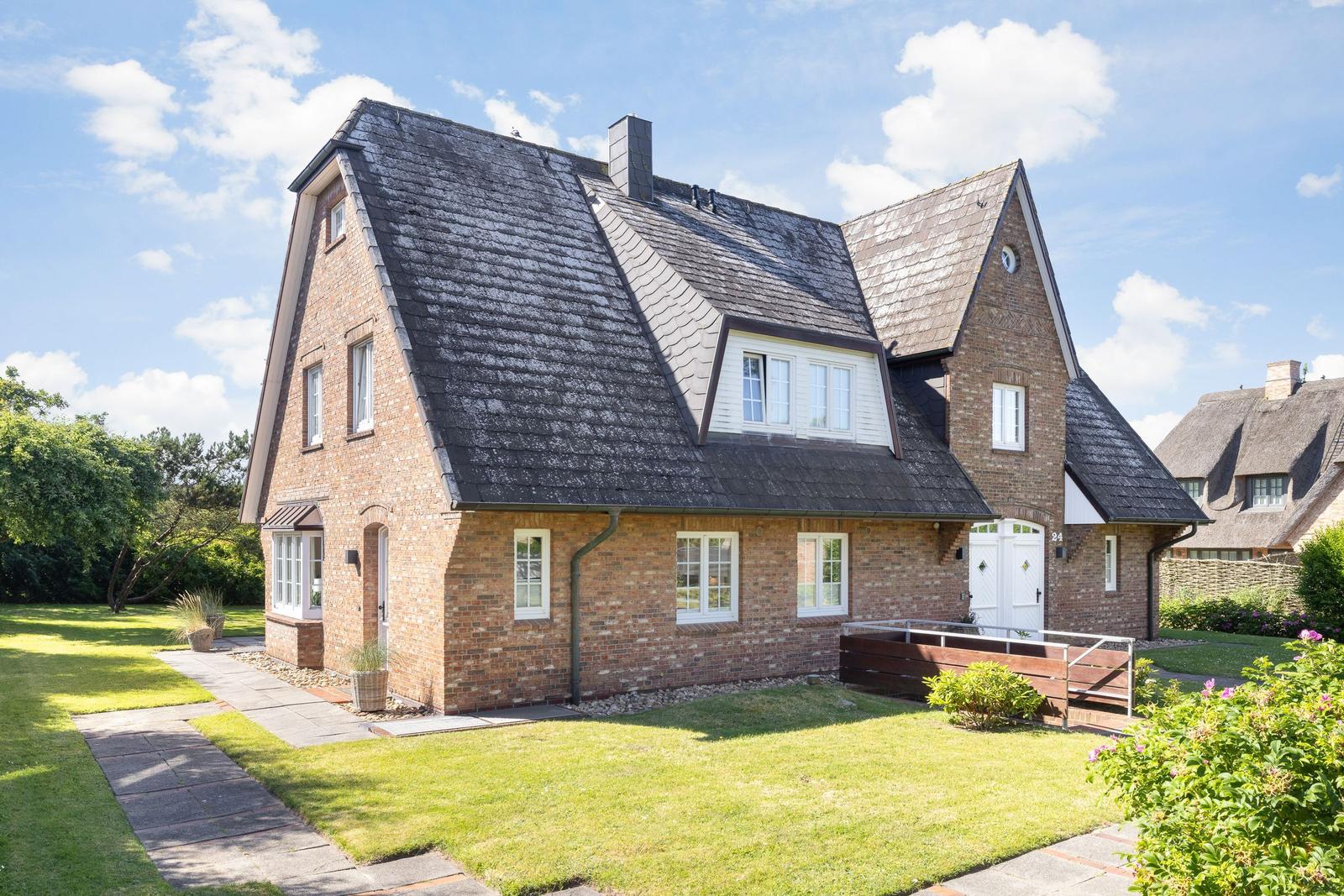 House with brick facade, dark roof, and white entrance. Lawn and paved path.