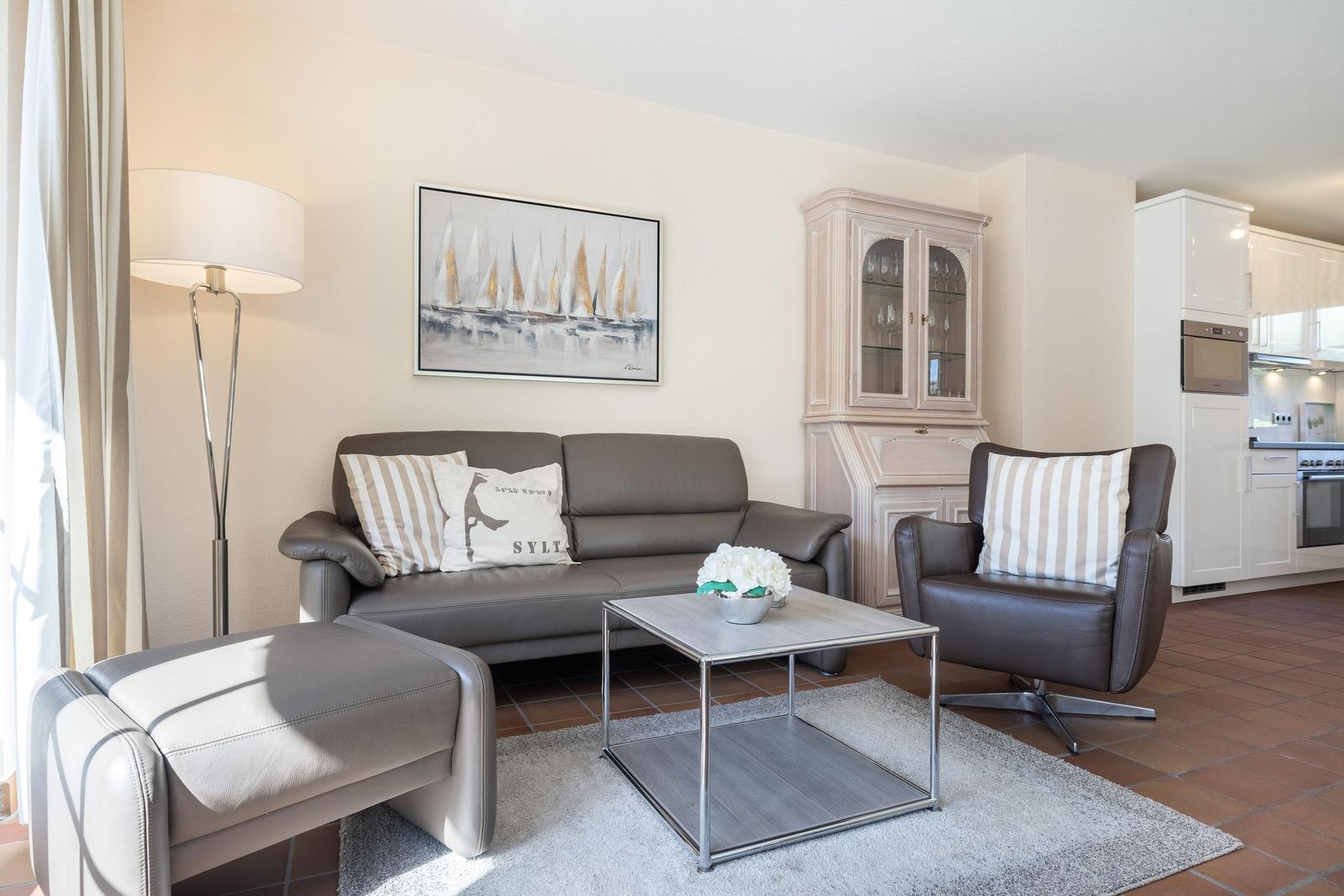 Living room with sofa, armchair, and coffee table. Kitchen in background.