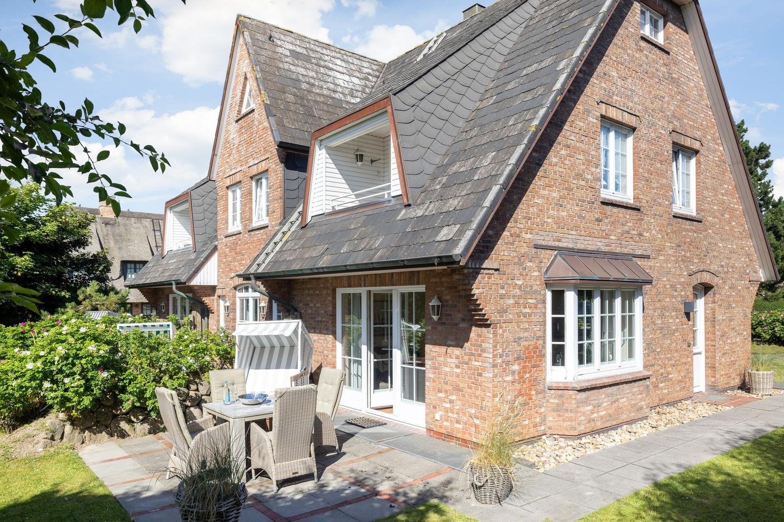 Red brick house with terrace and garden. White windows and dormers.