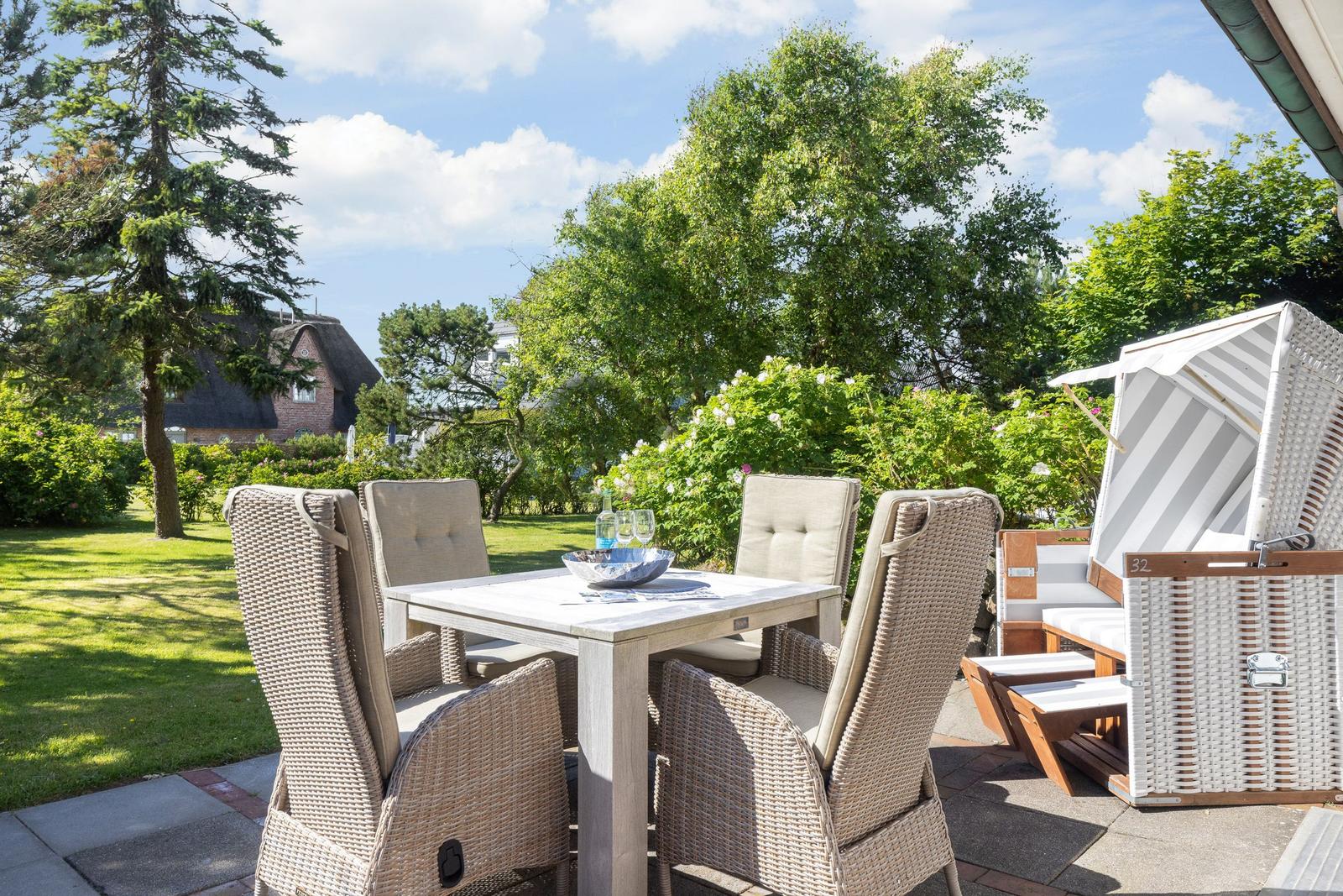 Terrace with dining table, chairs, and beach chair. Lawn and trees in background.