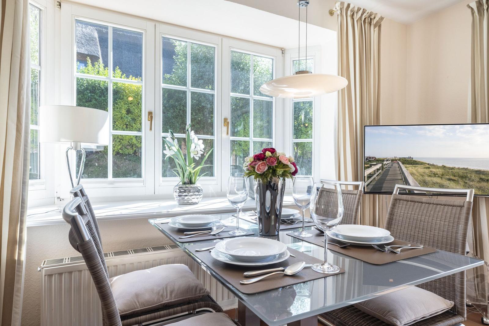 Dining table with chairs, flowers, and garden view through windows