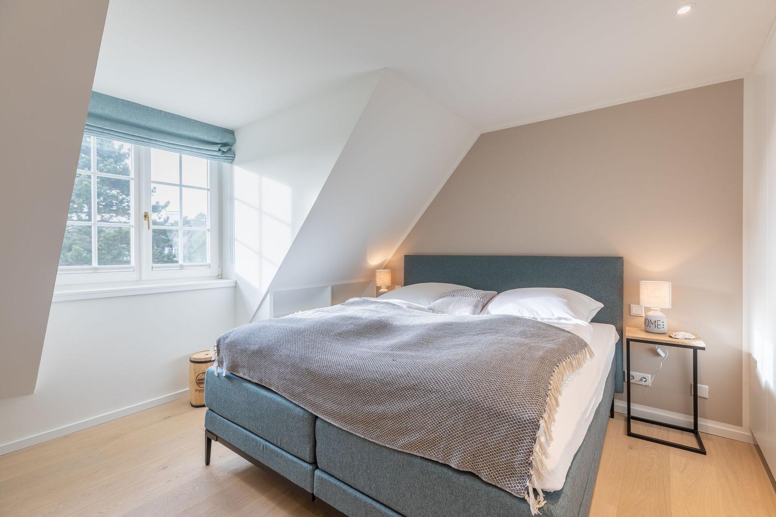 Bedroom with dormer window, bed, and bedside table.