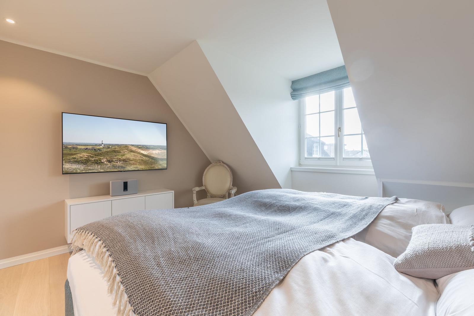Bedroom with sloped ceiling, bed, window, and TV mounted on the wall.